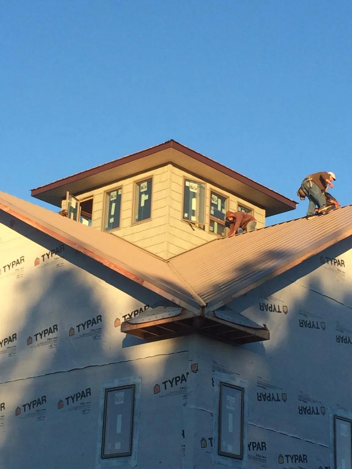 Roofers working around a rooftop cupola on a new metal roof at sunset — Roof Waterproofing in Logan by Roofing Brothers